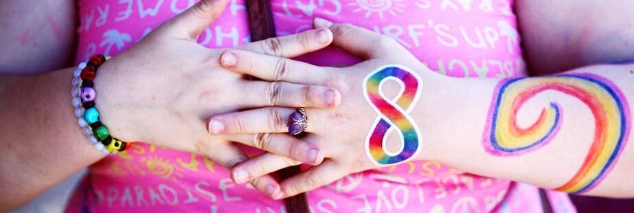 A woman displaying rainbow body paint and holding hands symbolizing diversity and inclusion